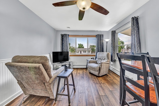 living area with ceiling fan, a wealth of natural light, baseboard heating, and dark wood-type flooring