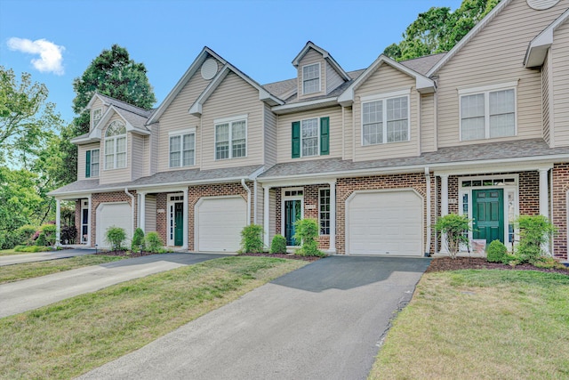 townhome / multi-family property featuring a shingled roof, an attached garage, a front lawn, brick siding, and driveway