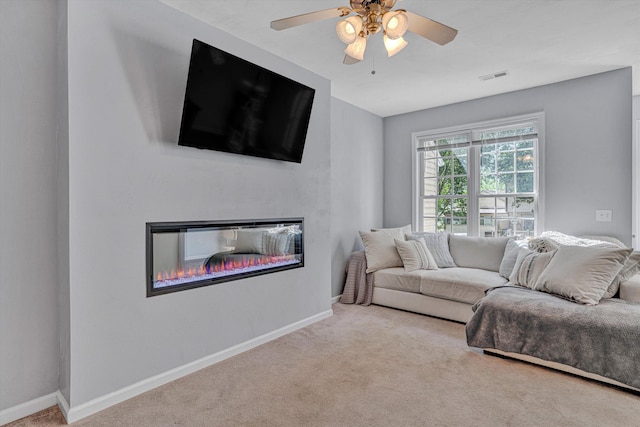 carpeted living room with ceiling fan, visible vents, a glass covered fireplace, and baseboards