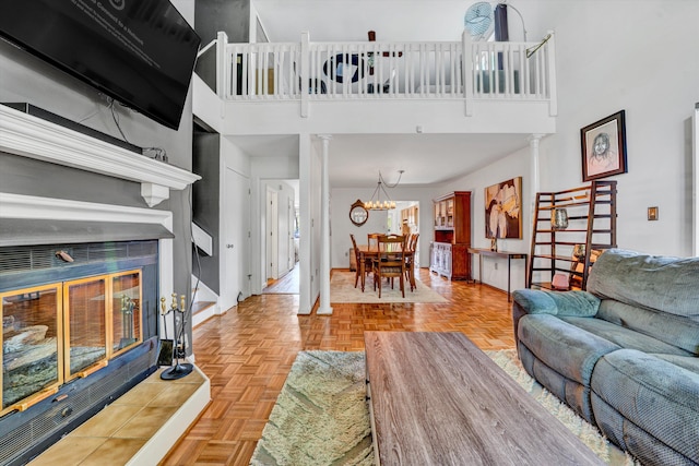 living area featuring decorative columns, a towering ceiling, a tiled fireplace, baseboards, and an inviting chandelier