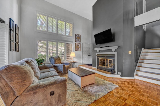 living room with stairs, a glass covered fireplace, a high ceiling, and a wealth of natural light