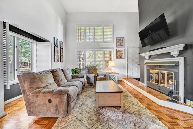 living area featuring a high ceiling, a glass covered fireplace, and baseboards