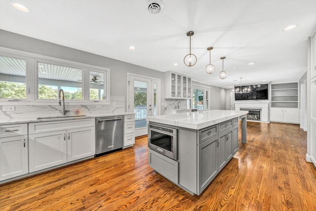 kitchen featuring stainless steel appliances, a sink, gray cabinetry, dark wood-type flooring, and glass insert cabinets