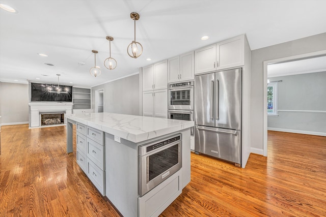 kitchen featuring stainless steel appliances, a fireplace, a kitchen island, wood finished floors, and recessed lighting