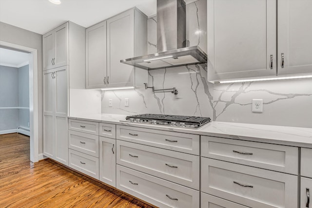 kitchen with wall chimney exhaust hood, decorative backsplash, light wood-style flooring, stainless steel gas stovetop, and light stone counters