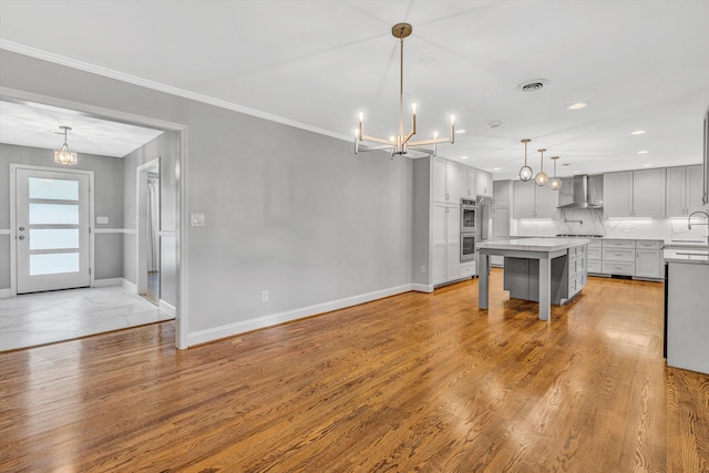 kitchen featuring wall chimney range hood, a chandelier, baseboards, a sink, and recessed lighting