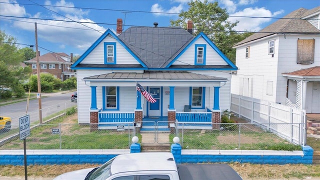 bungalow-style home with covered porch, a standing seam roof, a fenced front yard, metal roof, and a chimney