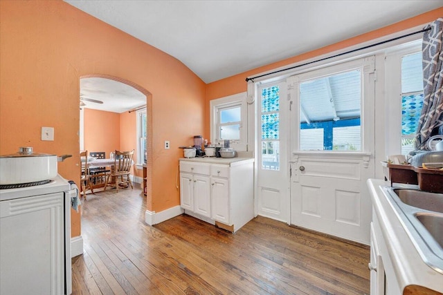 kitchen featuring light wood-type flooring, light countertops, white cabinetry, arched walkways, and vaulted ceiling