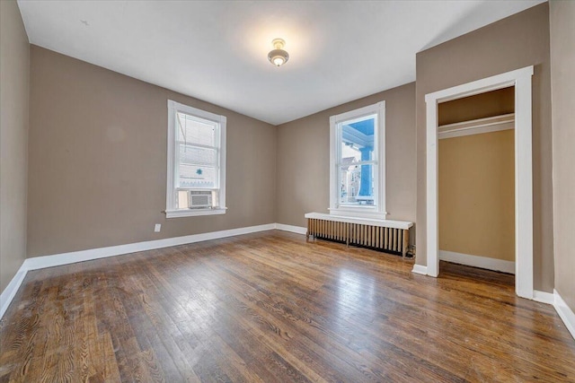 unfurnished bedroom featuring wood finished floors, baseboards, radiator heating unit, and cooling unit