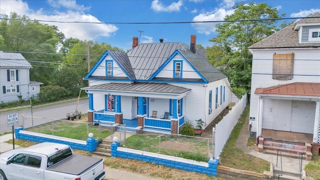 view of front of property with a chimney, a standing seam roof, metal roof, a porch, and a fenced front yard