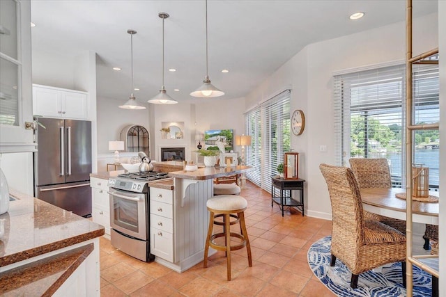 kitchen featuring recessed lighting, a glass covered fireplace, white cabinetry, a kitchen breakfast bar, and stainless steel appliances