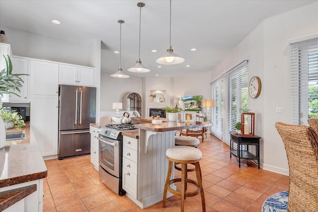 kitchen with stainless steel appliances, a kitchen bar, a glass covered fireplace, and white cabinets