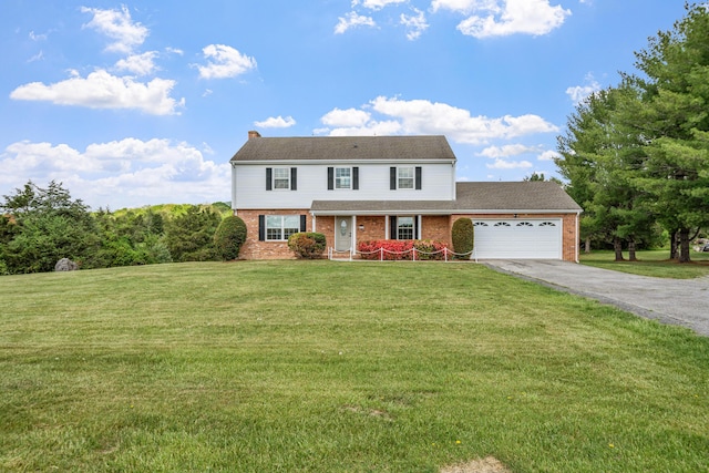 colonial-style house with a porch, aphalt driveway, an attached garage, brick siding, and a front yard