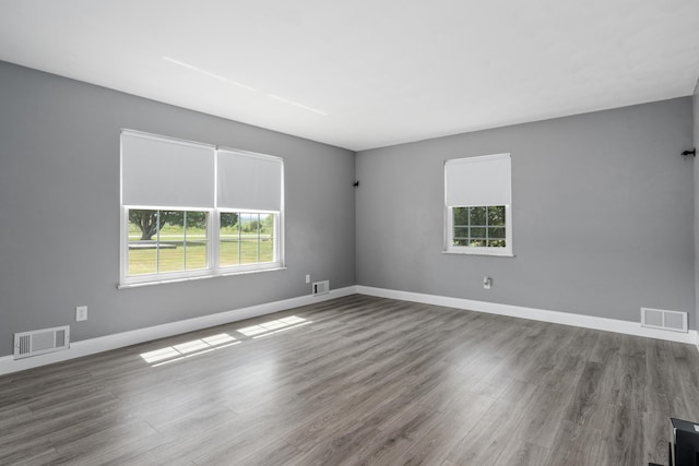 empty room with a wealth of natural light, visible vents, and wood finished floors