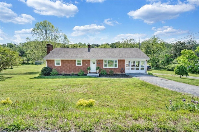 single story home with a chimney, gravel driveway, a front lawn, and brick siding