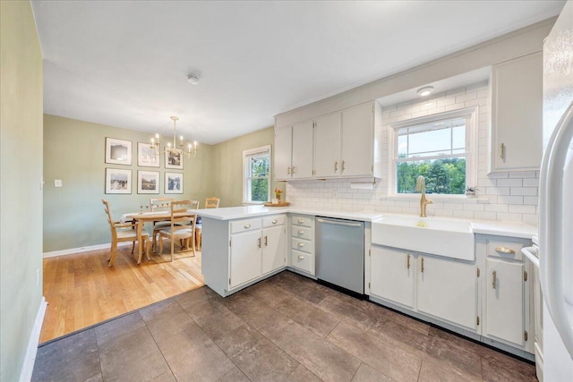 kitchen with tasteful backsplash, stainless steel dishwasher, a sink, a peninsula, and a notable chandelier