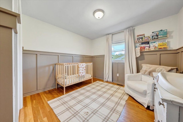 bedroom featuring wainscoting, wood finished floors, and a decorative wall