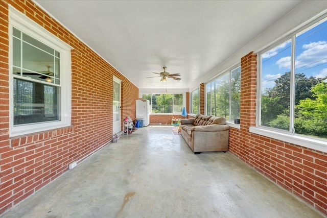 sunroom featuring a ceiling fan, brick wall, and unfinished concrete flooring