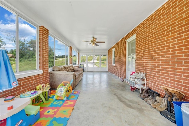 sunroom featuring ceiling fan, concrete floors, and brick wall