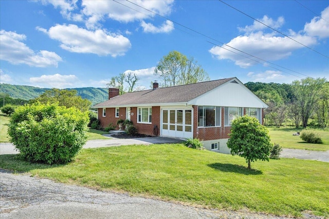 single story home featuring brick siding, a chimney, a front yard, and aphalt driveway