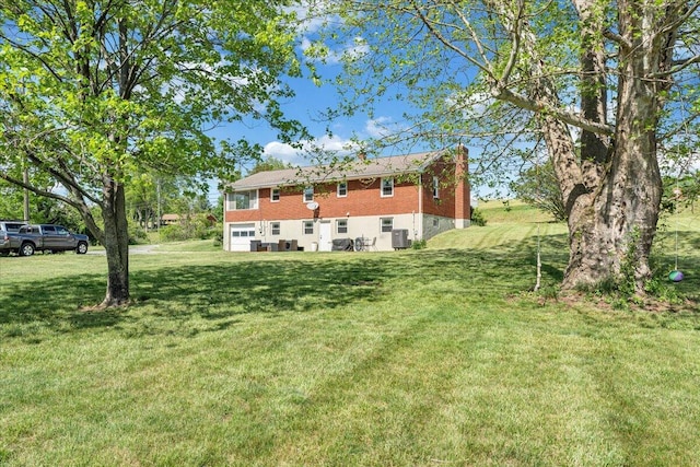 rear view of house featuring a garage, a chimney, a yard, and cooling unit