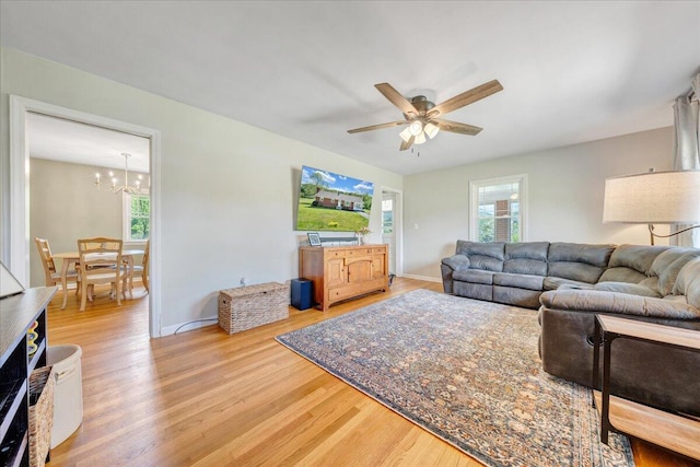 living room featuring baseboards, ceiling fan with notable chandelier, and light wood-type flooring
