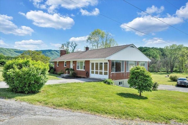 ranch-style home with brick siding, a front lawn, driveway, and a chimney