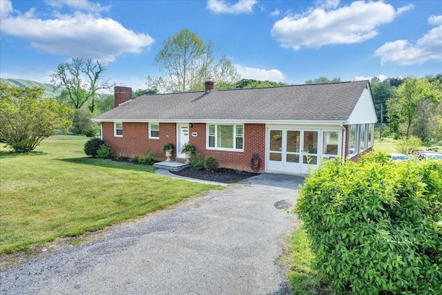 single story home with a chimney, brick siding, aphalt driveway, a shingled roof, and a front lawn