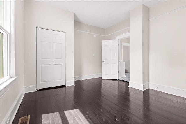 unfurnished bedroom featuring baseboards, dark wood finished floors, visible vents, and a closet