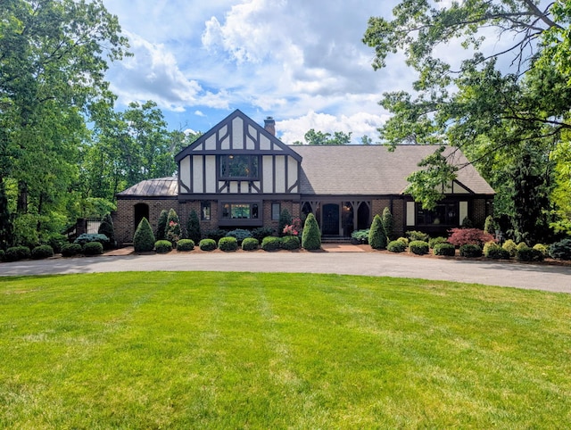 tudor house with a chimney, aphalt driveway, brick siding, and a front yard