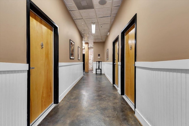 hallway with an ornate ceiling, wainscoting, and concrete floors