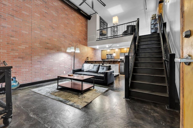 living room featuring stairs, brick wall, concrete floors, and a towering ceiling