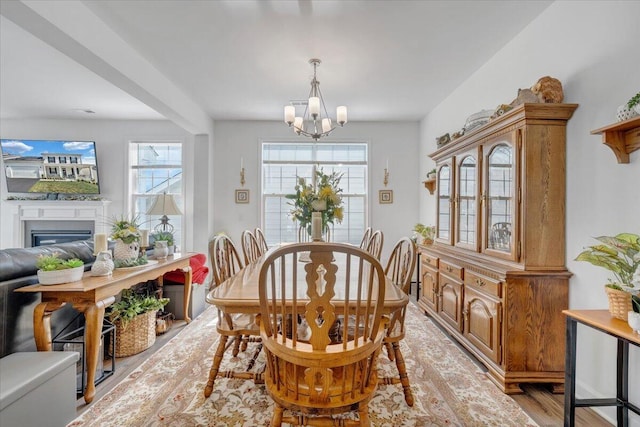 dining area with an inviting chandelier, a glass covered fireplace, and light wood-style floors