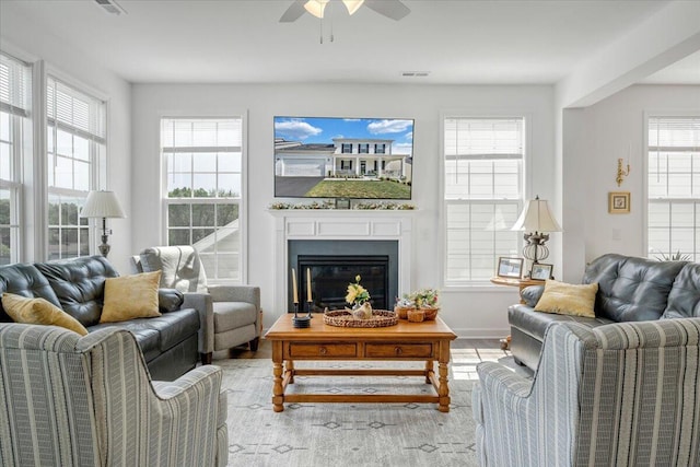 living room featuring a ceiling fan, visible vents, wood finished floors, baseboards, and a glass covered fireplace