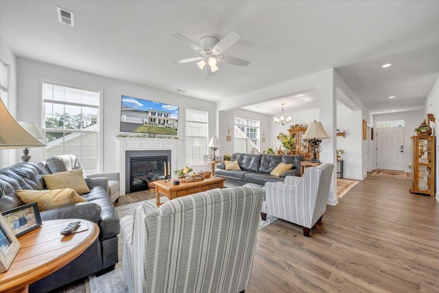 living room with visible vents, wood finished floors, ceiling fan with notable chandelier, a glass covered fireplace, and recessed lighting