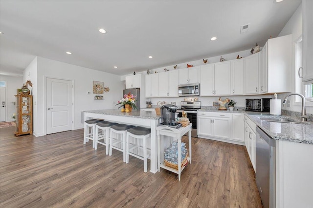 kitchen with a kitchen breakfast bar, a kitchen island, a sink, stainless steel appliances, and white cabinetry