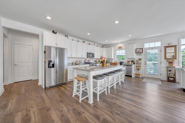kitchen featuring dark wood-style flooring, appliances with stainless steel finishes, a kitchen breakfast bar, a center island, and white cabinetry