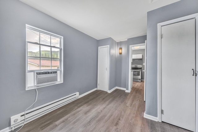 unfurnished bedroom with baseboard heating, wood finished floors, baseboards, and cooling unit