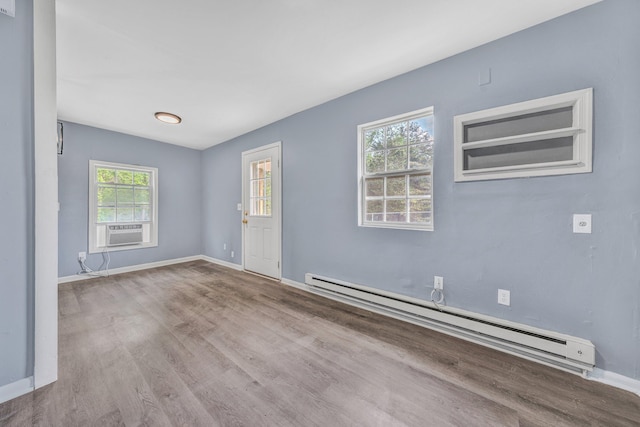 spare room featuring a baseboard radiator, wood finished floors, baseboards, and plenty of natural light