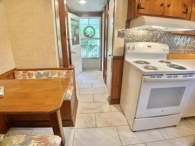 kitchen featuring brown cabinetry, light tile patterned flooring, under cabinet range hood, light countertops, and white range with electric stovetop
