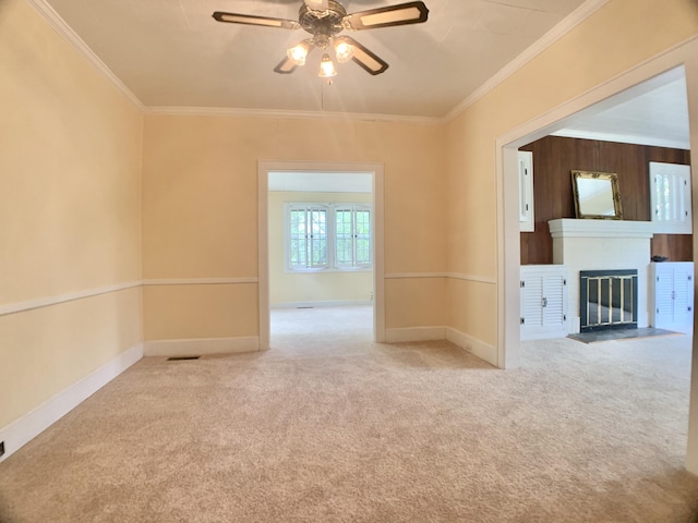 carpeted empty room with a ceiling fan, ornamental molding, a fireplace with flush hearth, and baseboards