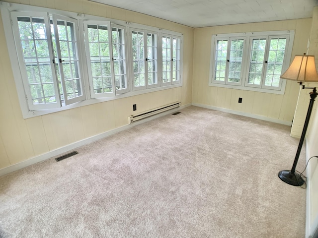 carpeted empty room with wooden walls, baseboards, baseboard heating, and visible vents