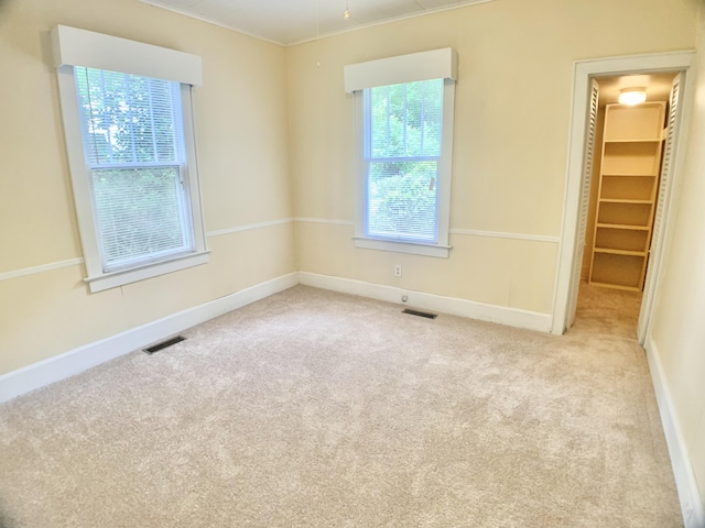 carpeted empty room with baseboards, crown molding, and visible vents