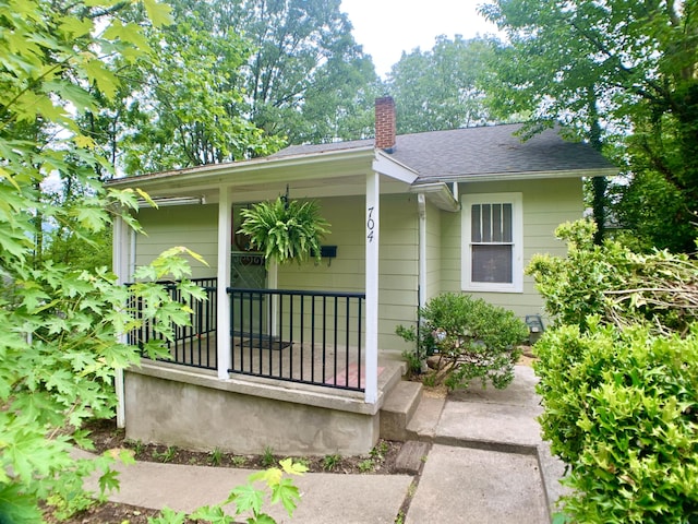 exterior space featuring covered porch, roof with shingles, and a chimney