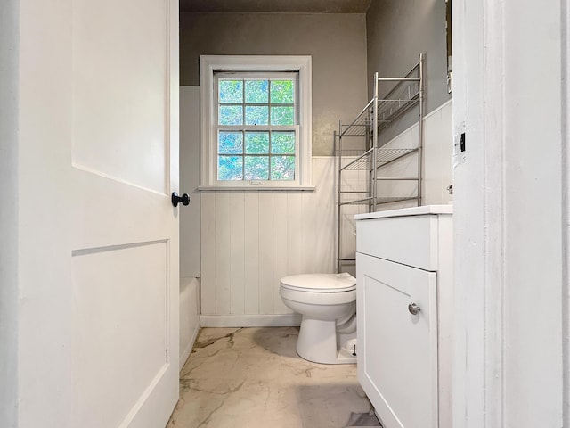 full bath featuring toilet, vanity, wainscoting, and a bathtub
