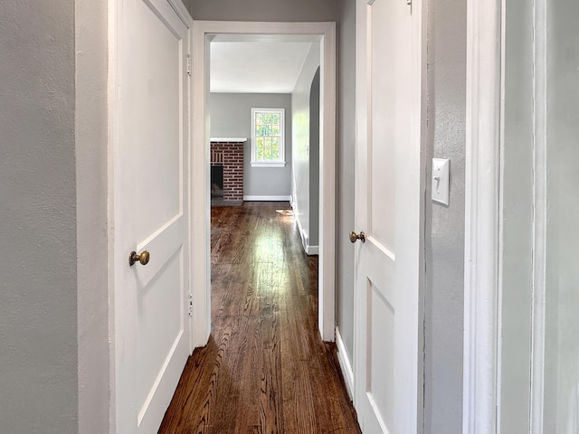 hall featuring dark wood-type flooring, baseboards, a textured wall, and arched walkways