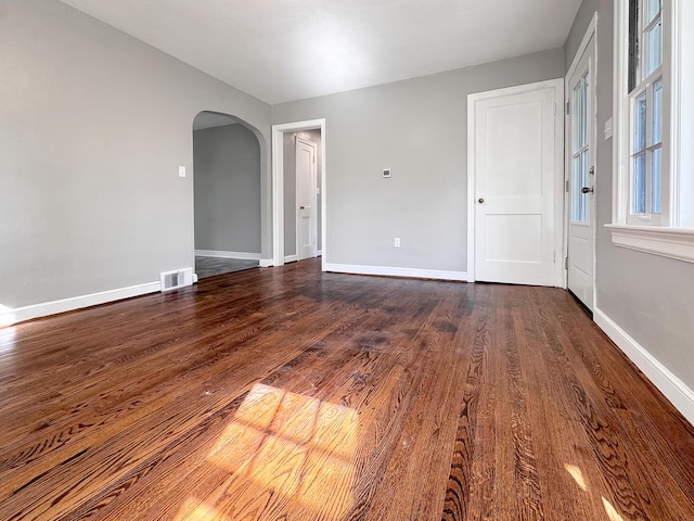 empty room with arched walkways, dark wood-style flooring, and baseboards