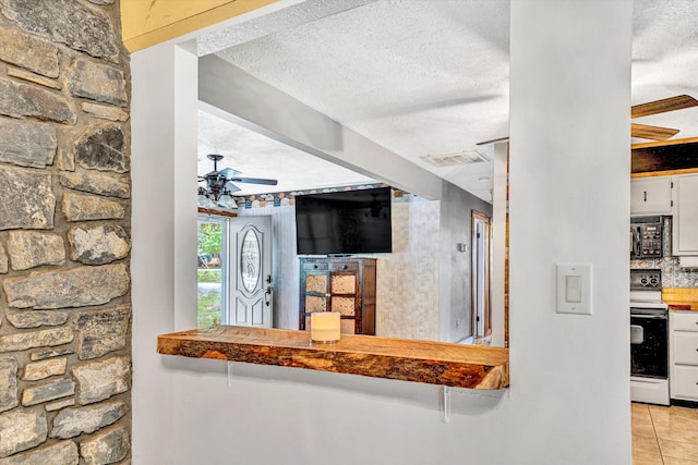 interior space with tile patterned flooring, black microwave, range with electric stovetop, a textured ceiling, and a ceiling fan