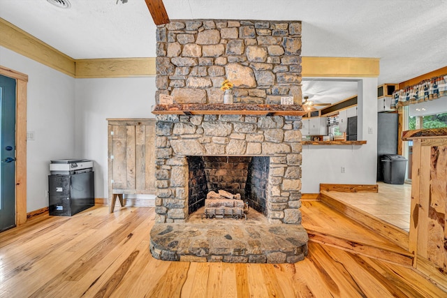 living room with a ceiling fan, a textured ceiling, a fireplace, wood finished floors, and baseboards