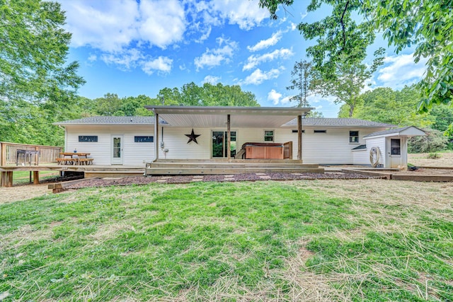 rear view of property with a deck, a lawn, a storage shed, a hot tub, and an outbuilding